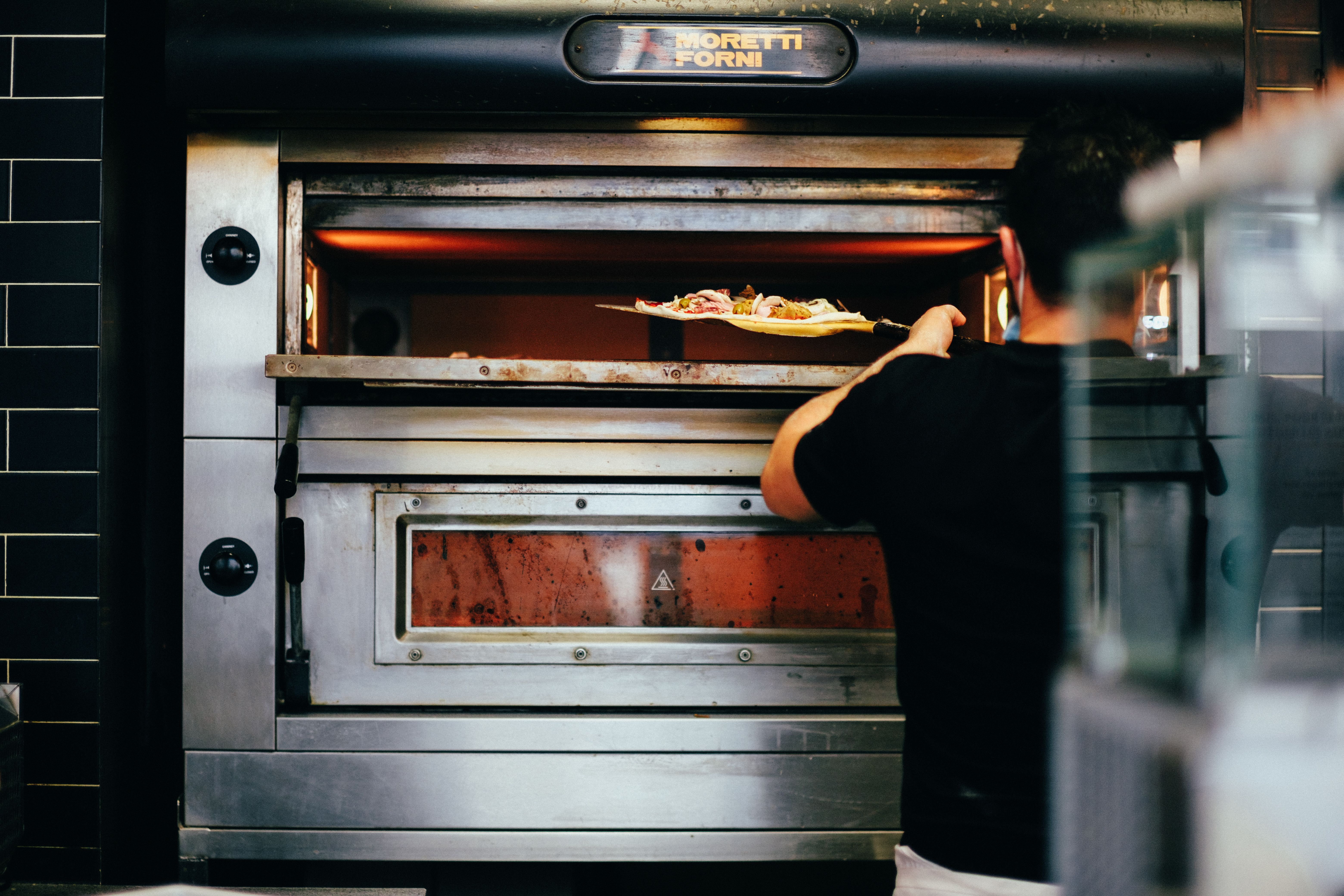 Cuisinier enfournant une pizza dans un four à pizza professionnel.